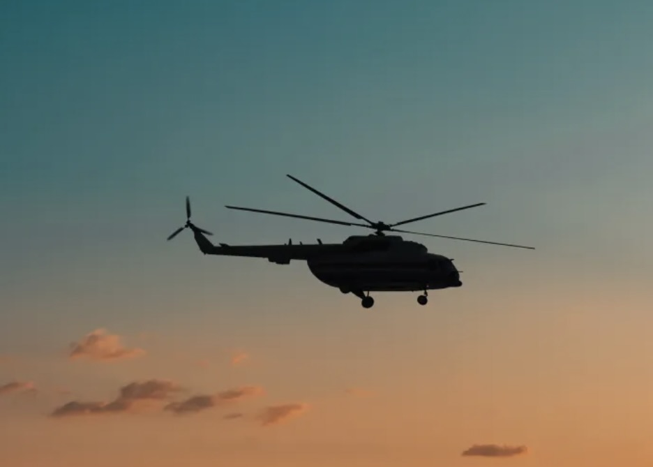 Helicopter flies in the mountains at sunset in the dark. 